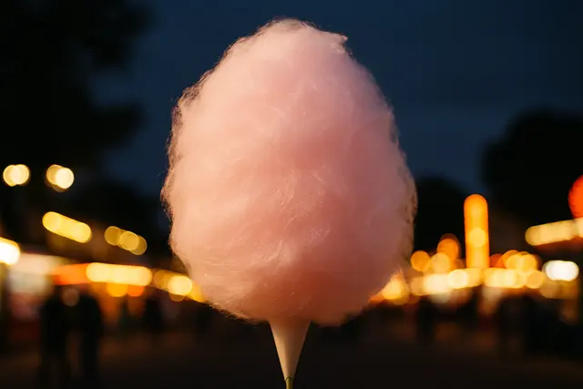 Large pink cloud of spun cotton candy on a paper cone against blurred fairground lights