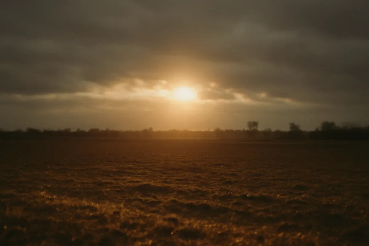 Low winter sun breaking through gray cloud, casting one bright band across a bare field
