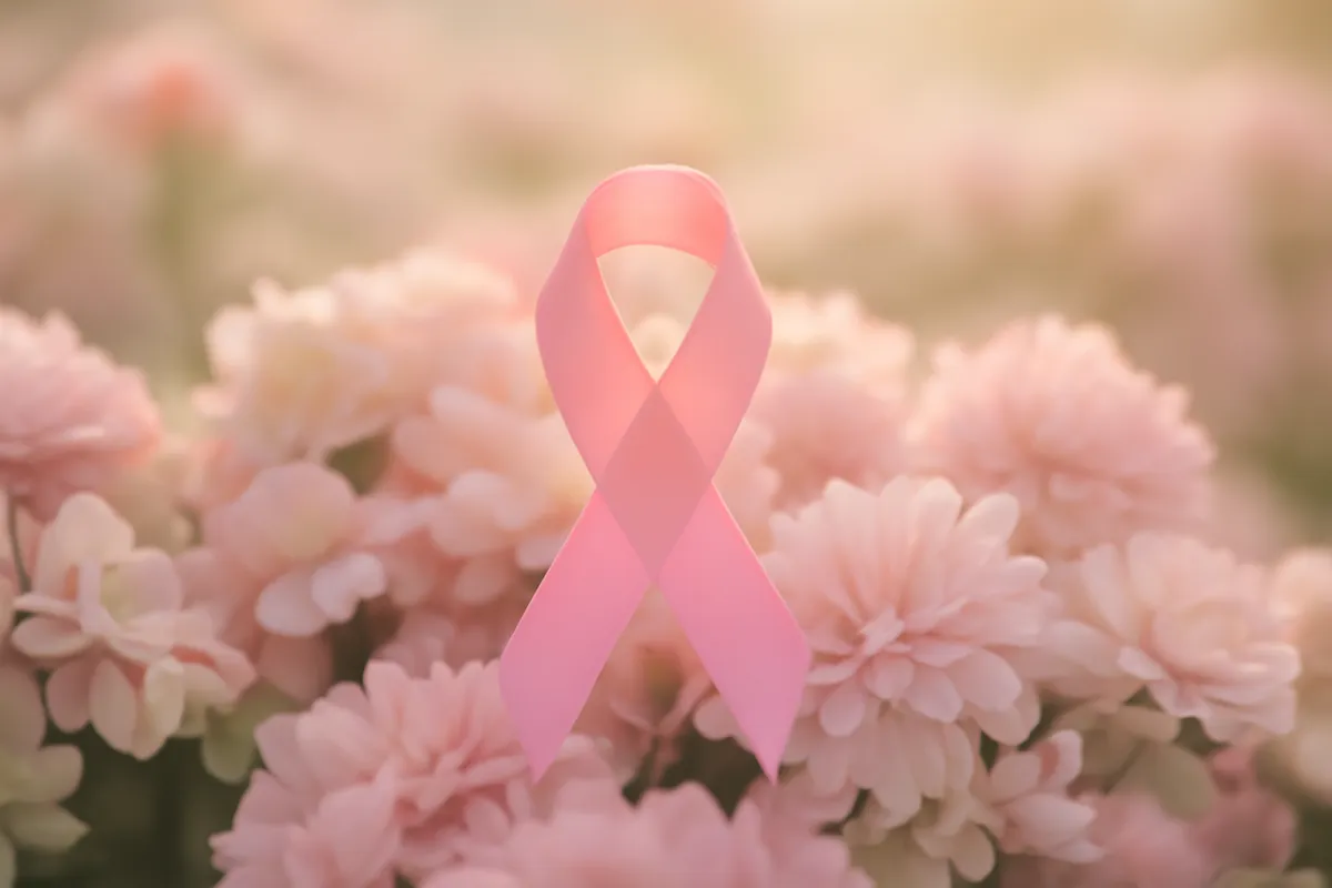 A pink awareness ribbon resting among soft pink and white flowers in morning light