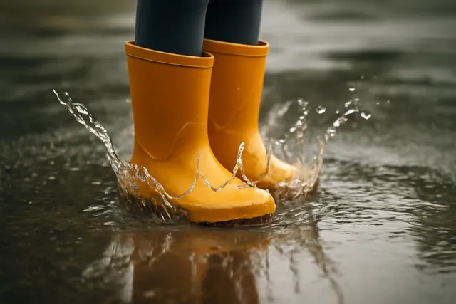 Rubber boots stamping in a puddle throwing up a crown of water on wet pavement