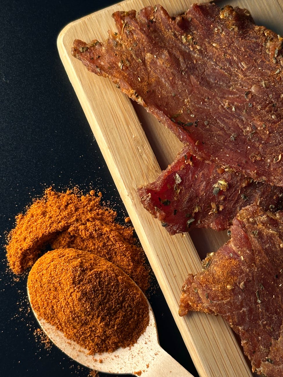 spoon of spice next to raw meat on a cutting board