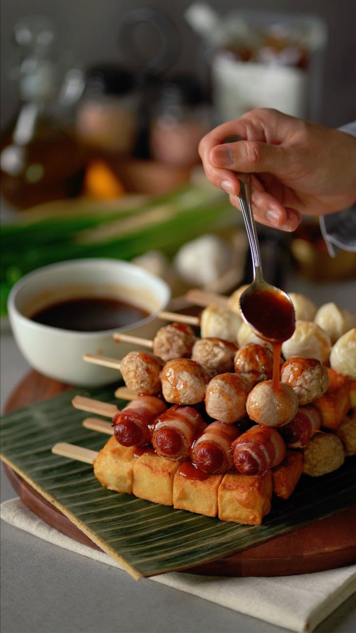cook pouring sauce over fish balls and kilted sausages on skewers