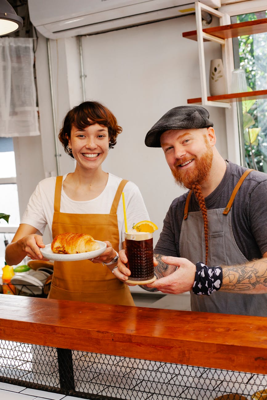 cheerful partners with tasty pastry and alcoholic drink at work